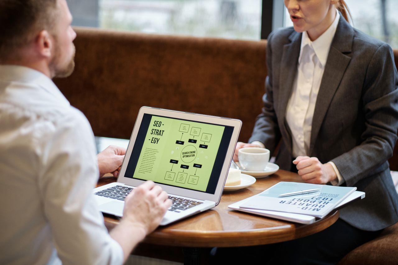 services-01 A man and woman engaged in a business meeting discussing SEO strategy in a cozy cafe setting.